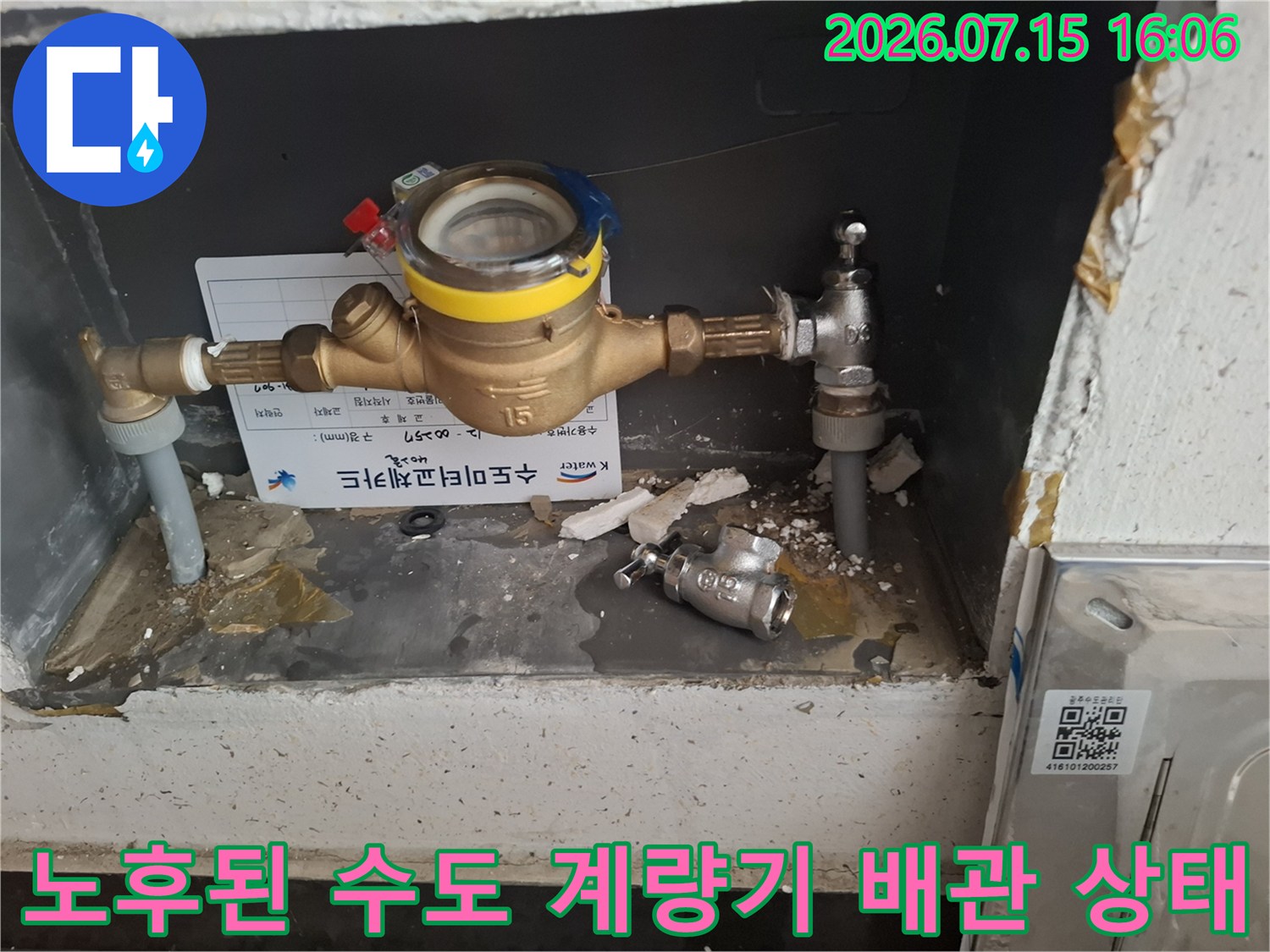 벽면함 속에 설치된 노란색 표시의 수도 계량기와 금속 배관 라인