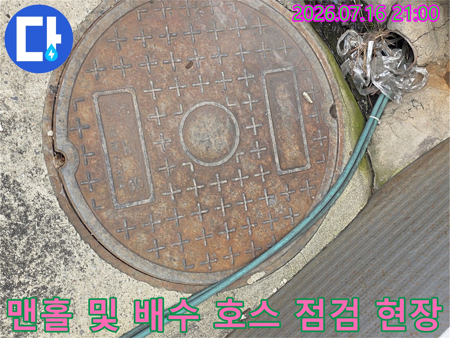 상가 로비 바닥에 위치한 맨홀과 노출된 청록색 외관의 배수용 연결관