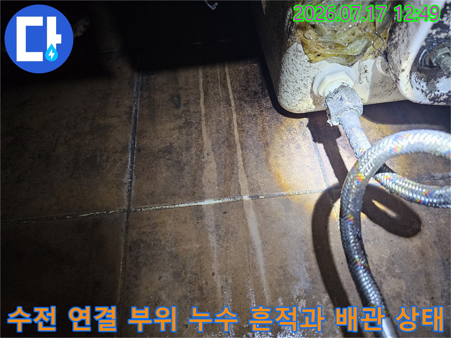 싱크대 아래 수전 호스의 노후된 모습과 주변 타일의 누수 오염 상태를 촬영한 사진