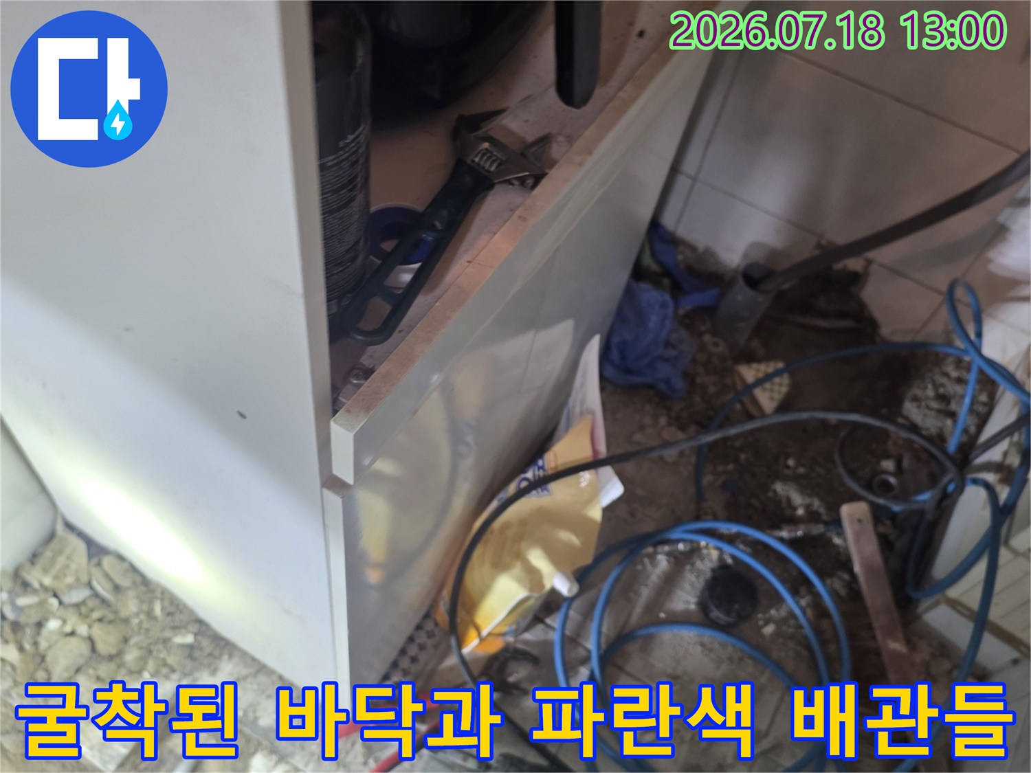 바닥 타일을 걷어내고 드러난 파란색 플라스틱 배관과 주변의 공구들-누수 수선 과정