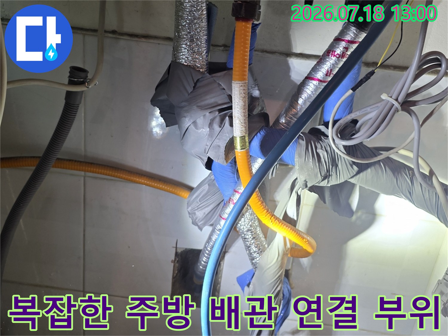 주방 싱크대 하단에 설치된 파란색과 노란색의 복합 배관 연결 상태-사진