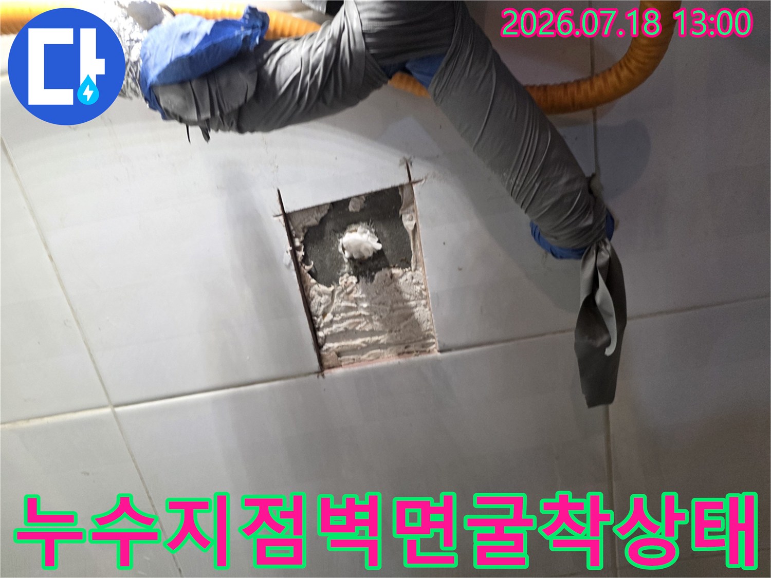 타일 벽면에 사각형 구멍을 내어 내부 시멘트 층과 배관 매립 부분을 드러낸 사진