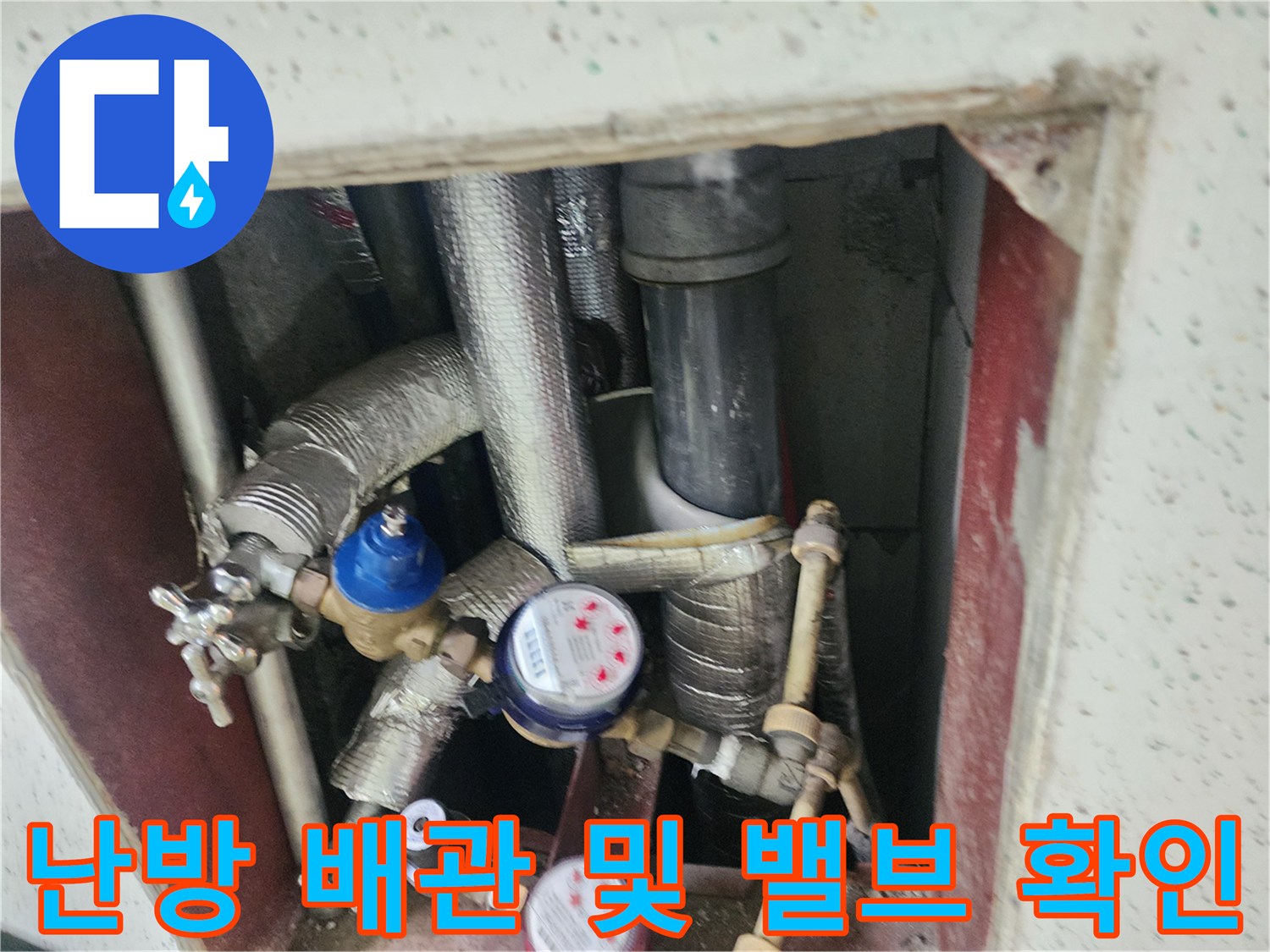 보온재로 감싸진 배관과 수치 확인을 위한 계량기가 보이는 싱크대 하단 내부 사진입니다.