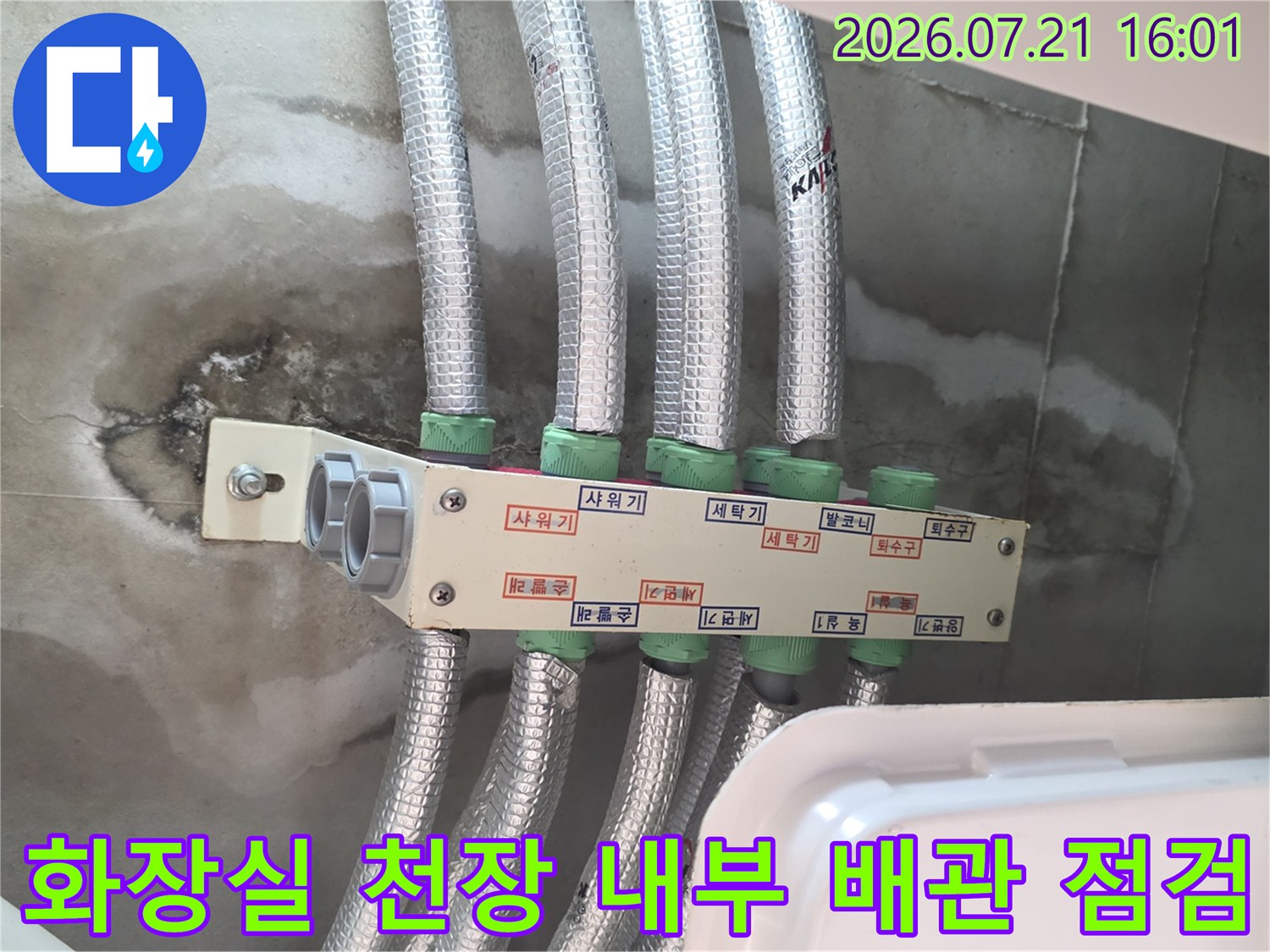 거친 벽면에 설치된 여러 개의 보온재 덮인 화장실 천장 배관들