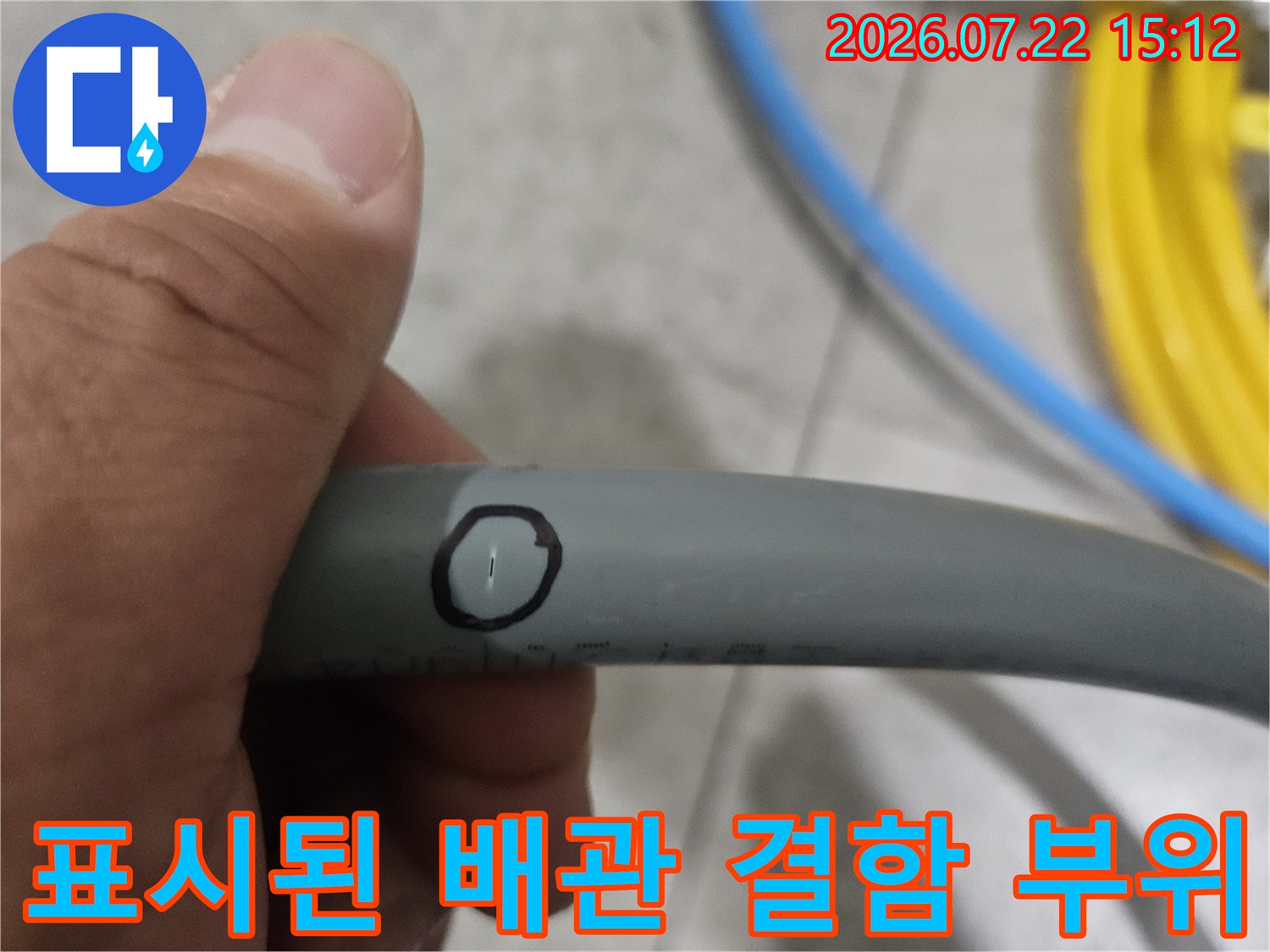 손으로 잡고 있는 회색 배관의 특정 지점에 누수 위치를 표시한 모습