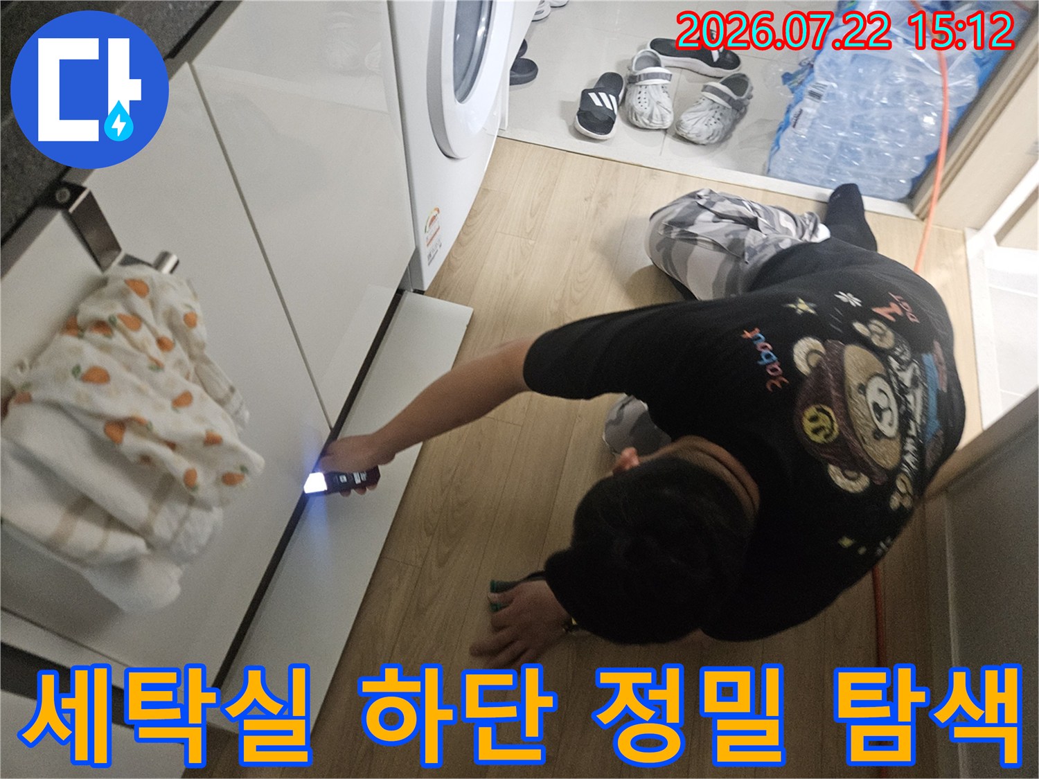 엔지니어가 세탁실 싱크대 하단 좁은 틈새를 손전등으로 비추며 누수 지점을 찾는 모습