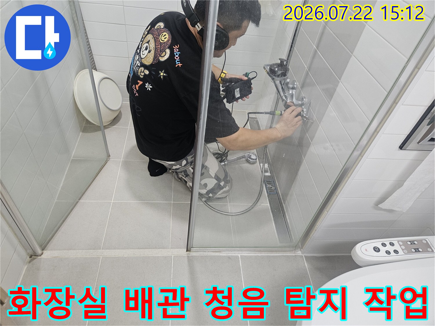 엔지니어가 헤드셋을 착용하고 화장실 벽면 수전 부위에서 청음 탐지기로 누수 지점을 찾는 모습