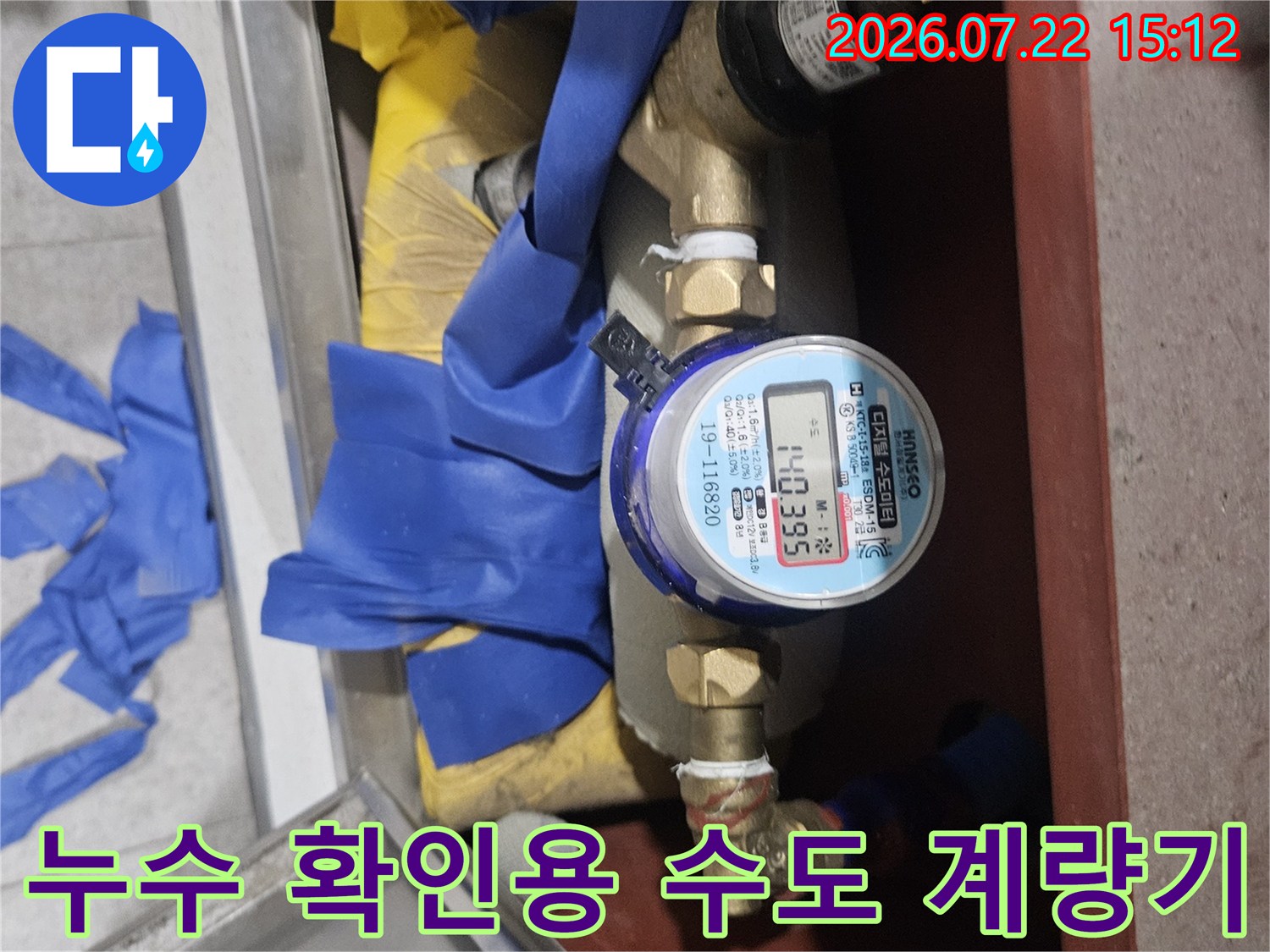 파란색 테이프로 보강된 배관과 그 중앙에 위치한 숫자 표시 수도 계량기 사진