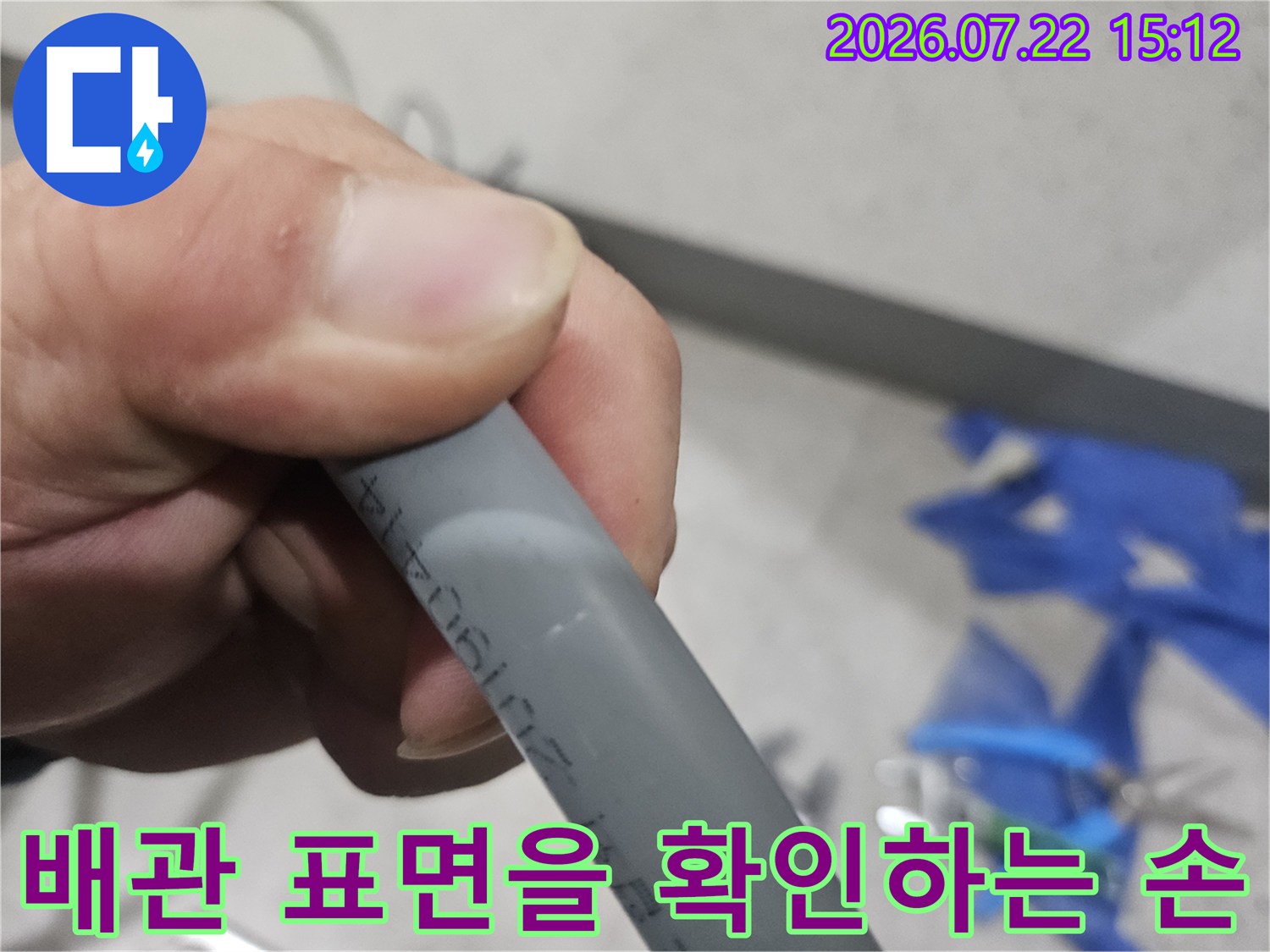 회색 플라스틱 수도 배관의 외관 상태를 손으로 짚어가며 점검 중인 사진