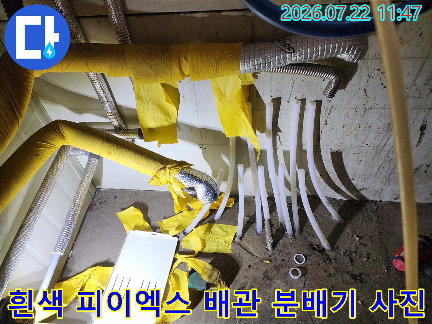 분배기에서 뻗어 나온 여러 개의 흰색 난방 배관과 일부 벗겨진 노란색 보온재 모습
