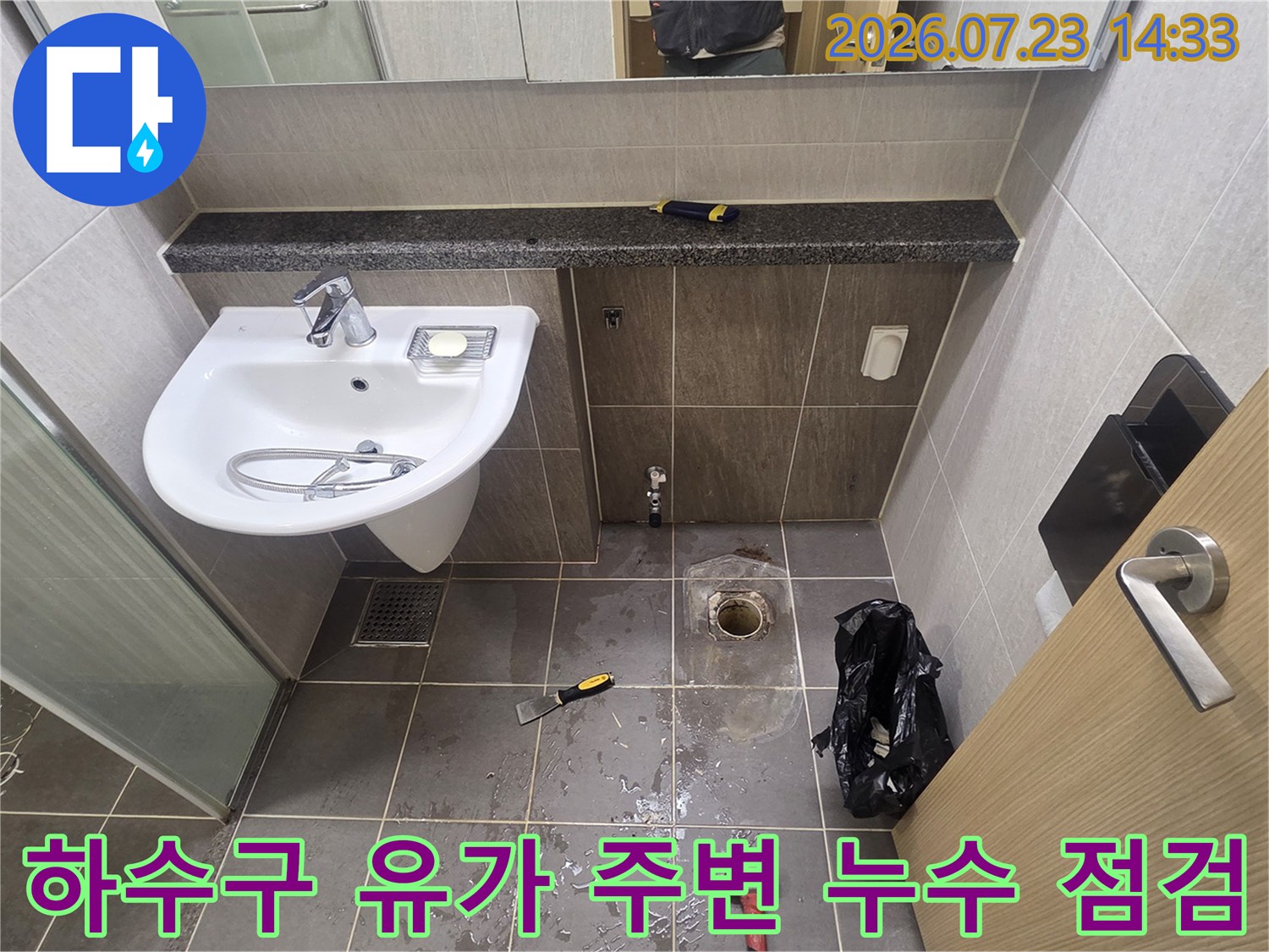 욕실 세면대 하단 배수구의 타일이 제거되어 내부 배관 구조가 노출된 사진