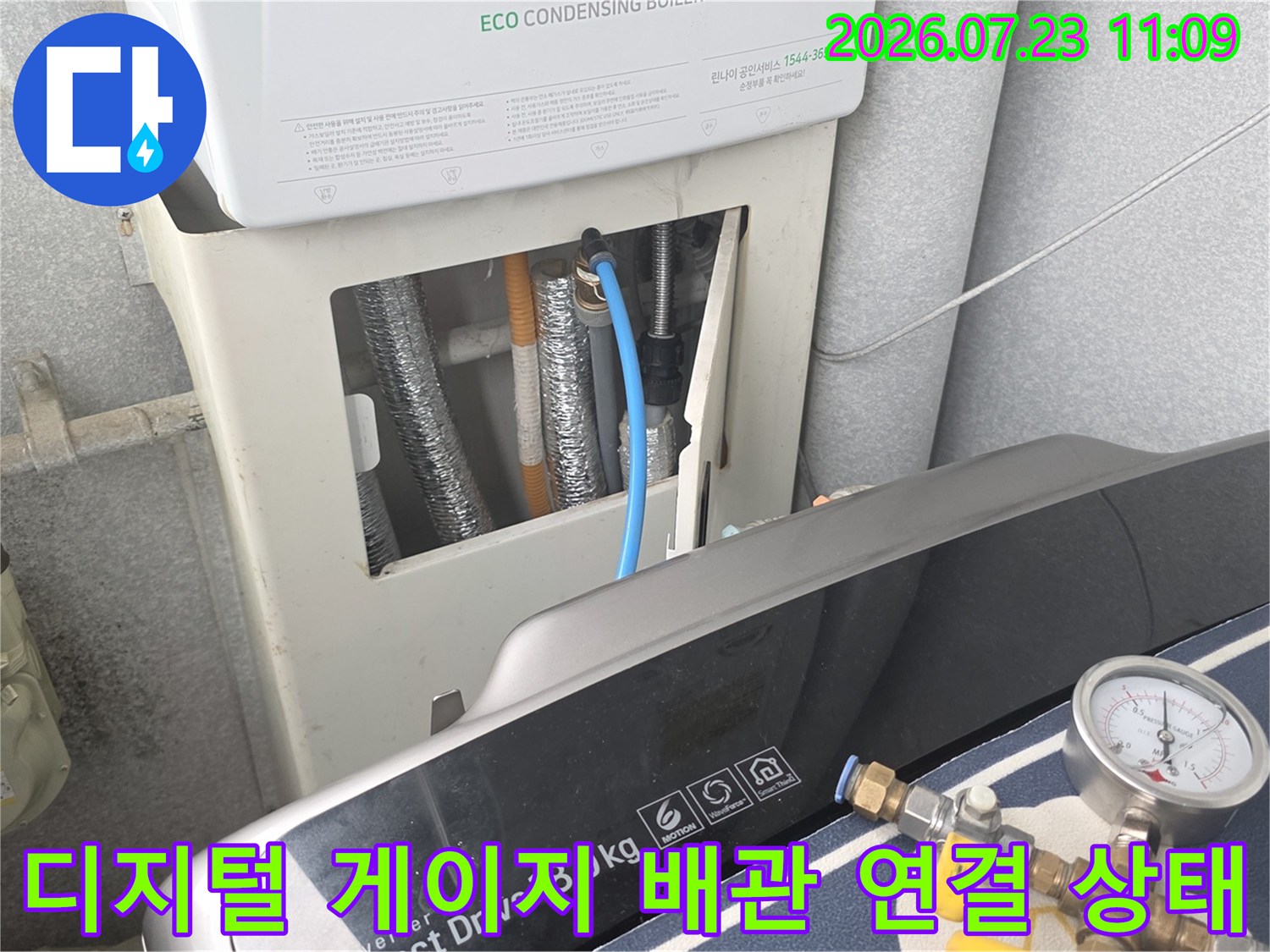 흰색 보일러 하부의 은색 단열재 배관과 파란색 호스가 연결된 압력계