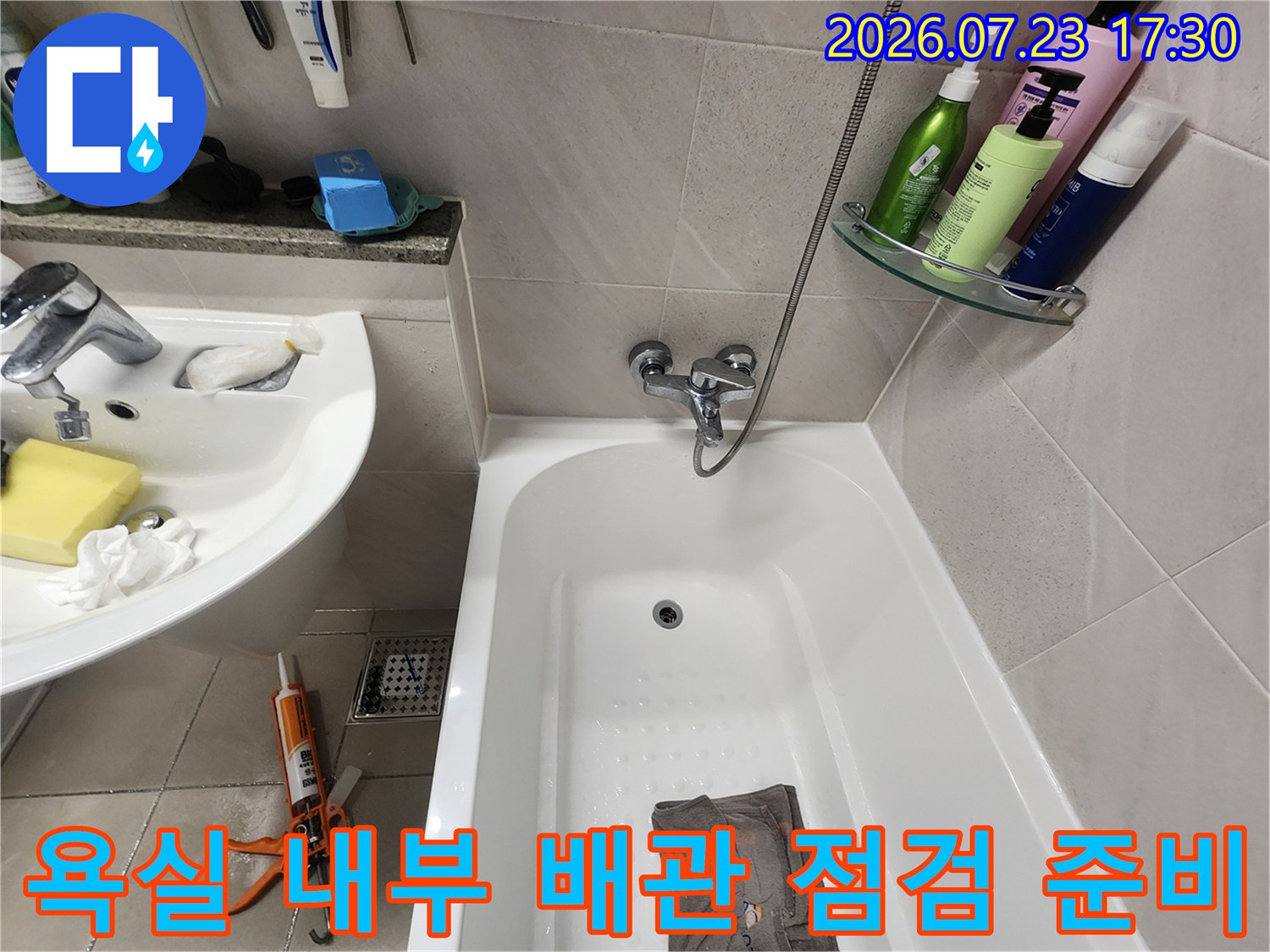 흰색 세면대와 욕조가 설치된 공간에 놓여 있는 주황색 렌치 공구