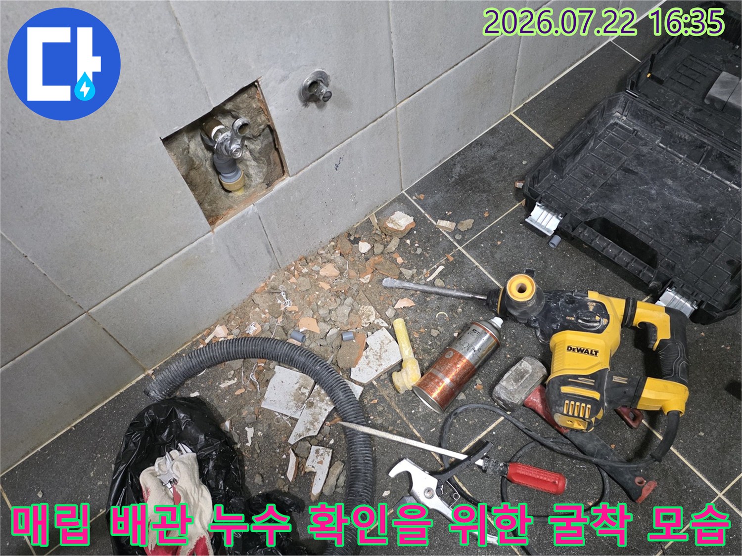 벽면 타일이 일부 제거되어 내부의 수도 밸브와 배관 연결부가 노출된 현장 사진-바닥에는 공구들이 흩어져 있음