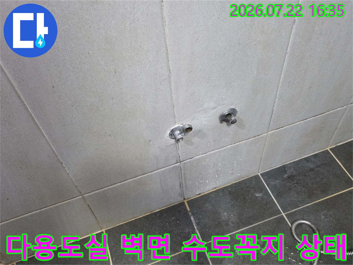 회색 타일 벽면에 설치된 수도꼭지와 바닥에 놓인 샤워 호스-누수 점검 전 모습