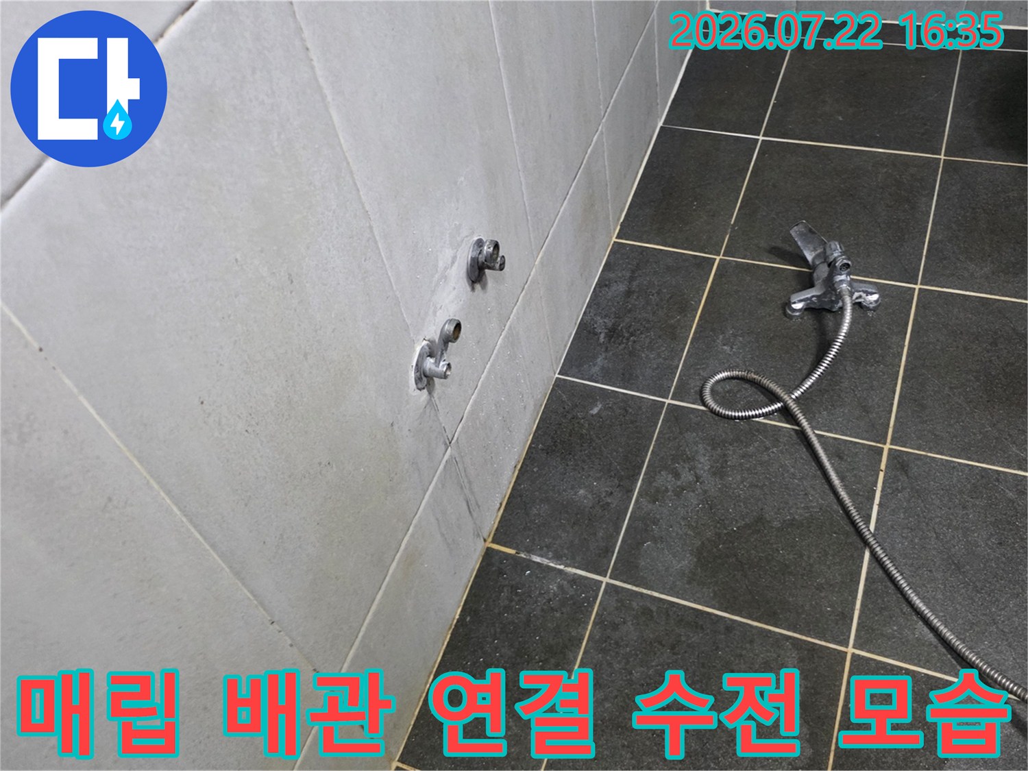 회색빛 타일 마감 벽면에 설치된 수도꼭지와 바닥의 금속제 샤워 호스-누수 진단 중