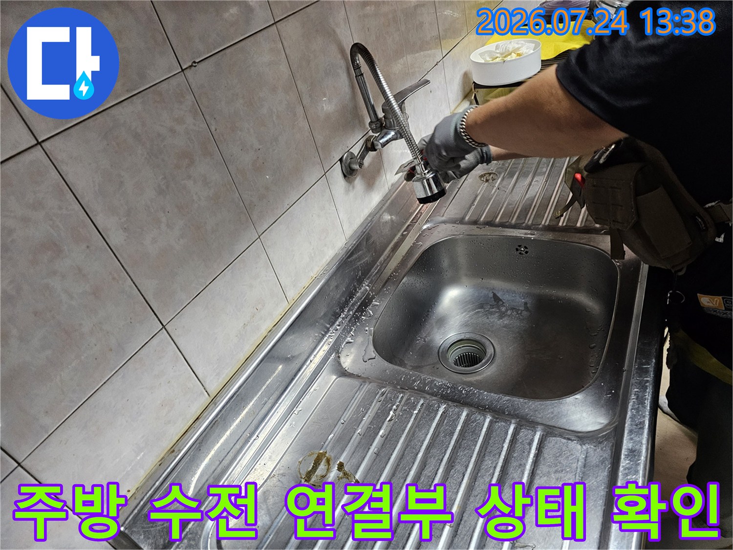 장갑을 낀 작업자가 스테인리스 싱크대 볼 위에서 수도꼭지 연결 부분을 점검하는 사진