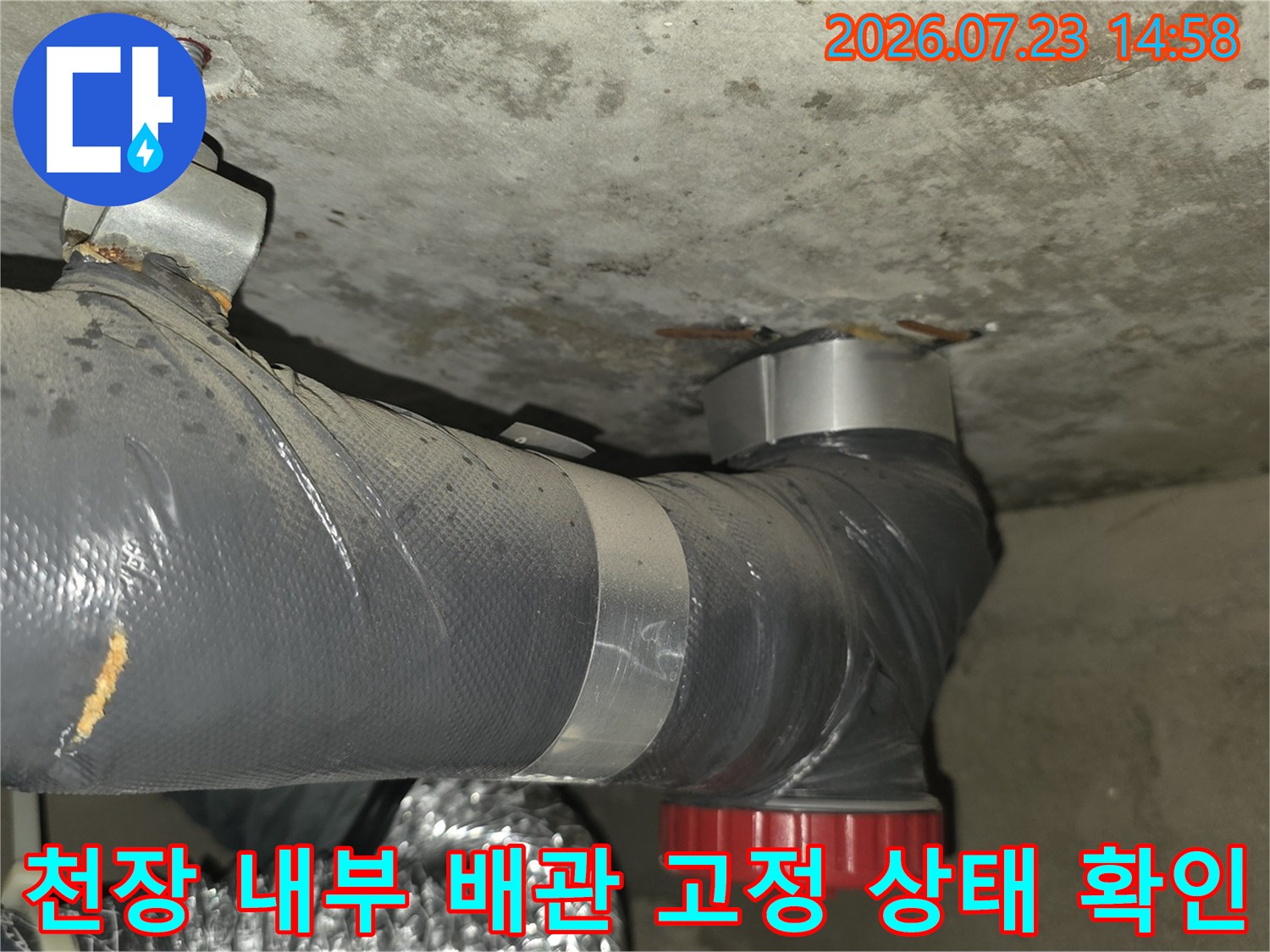 천장에 브라켓으로 고정된 회색 배관-하단 빨간색 부속 연결 모습