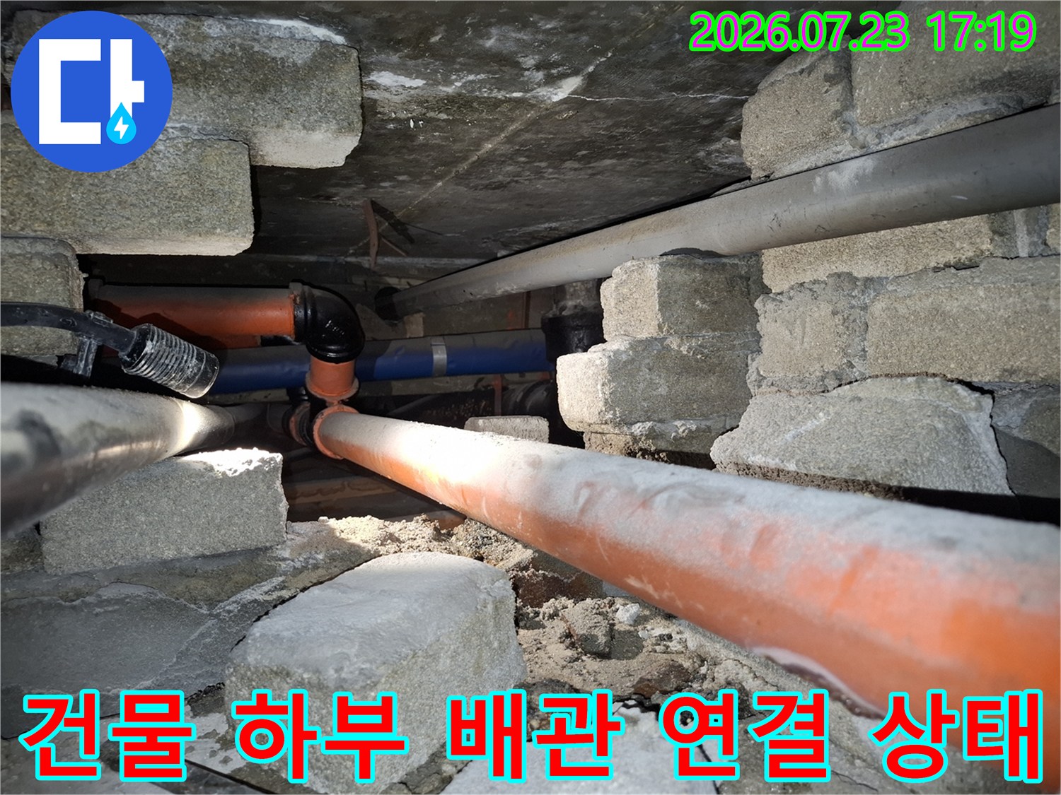 콘크리트 구조물 아래로 설치된 오렌지색과 파란색의 복합 배관 라인-누수 점검 모습