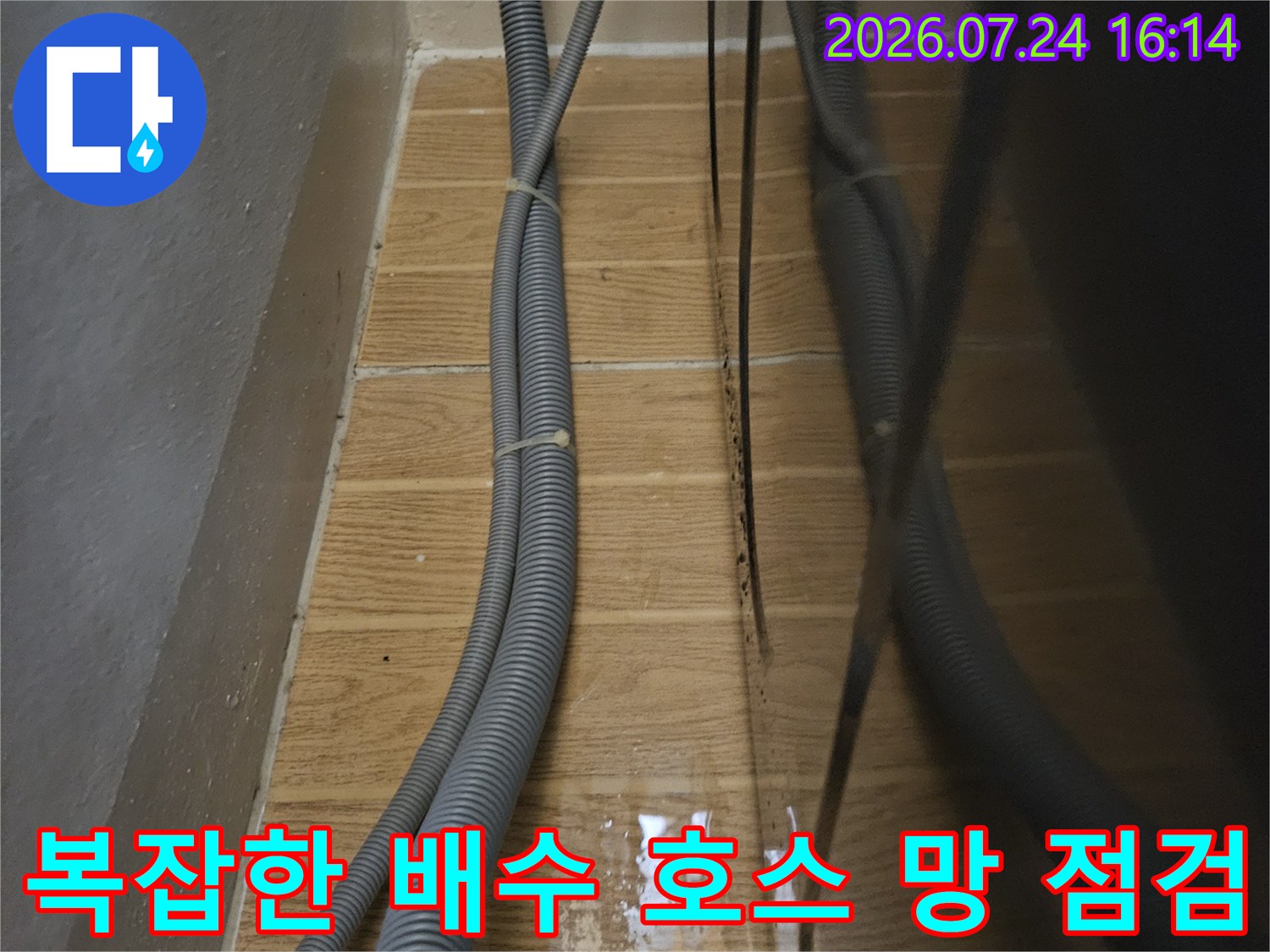 싱크대 아래 굴곡진 배수관들과 벽면 타일이 만나는 지점의 세부 모습