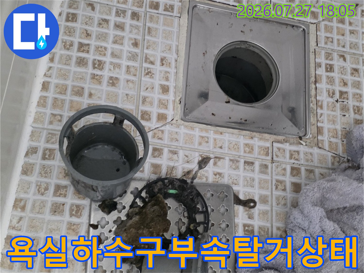 화장실 타일 위-분리된 하수구 거름망과 트랩이 놓여 있고 내부 배관이 노출된 모습