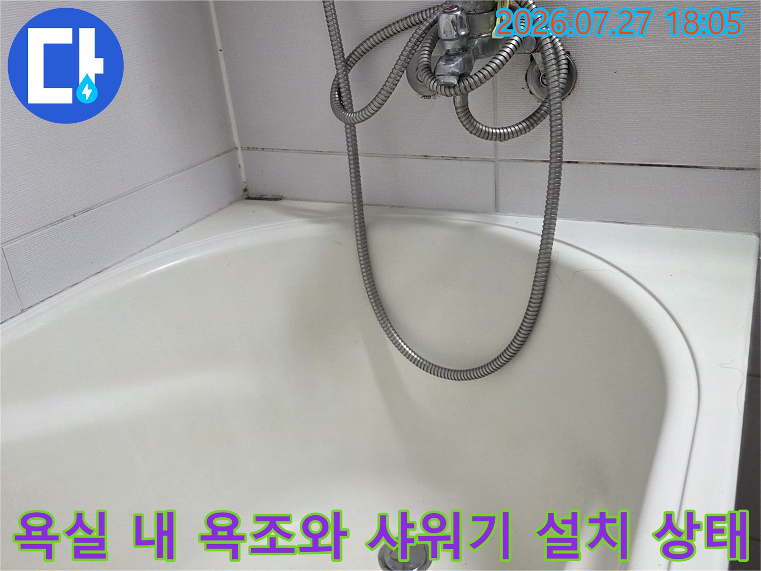 흰색 플라스틱 재질의 욕조와 그 위에 걸쳐진 금속제 샤워 호스