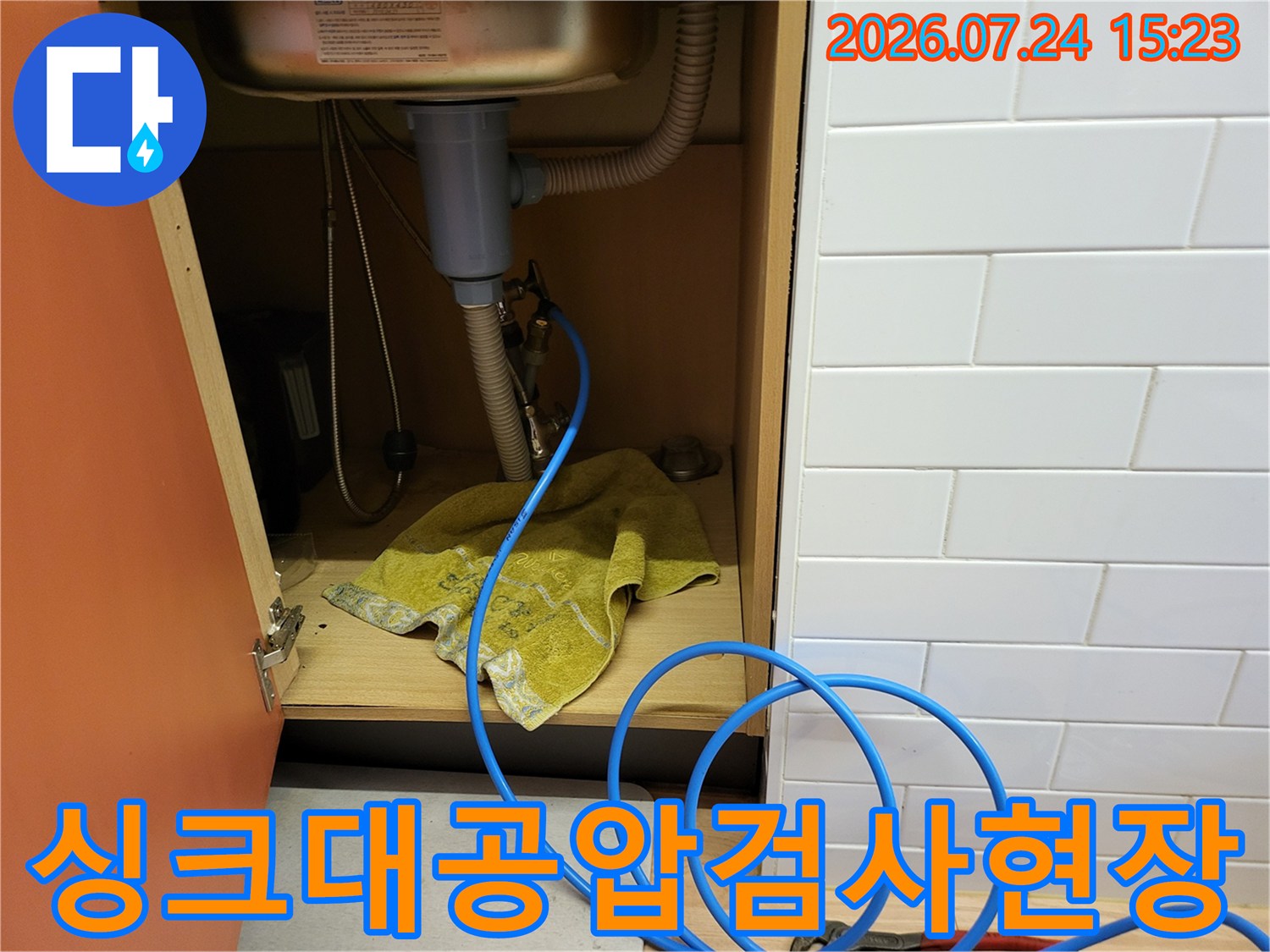 파란색 공압 테스트 호스가 싱크대 하단 배관에 연결되어 누수 진단이 이루어지는 장면