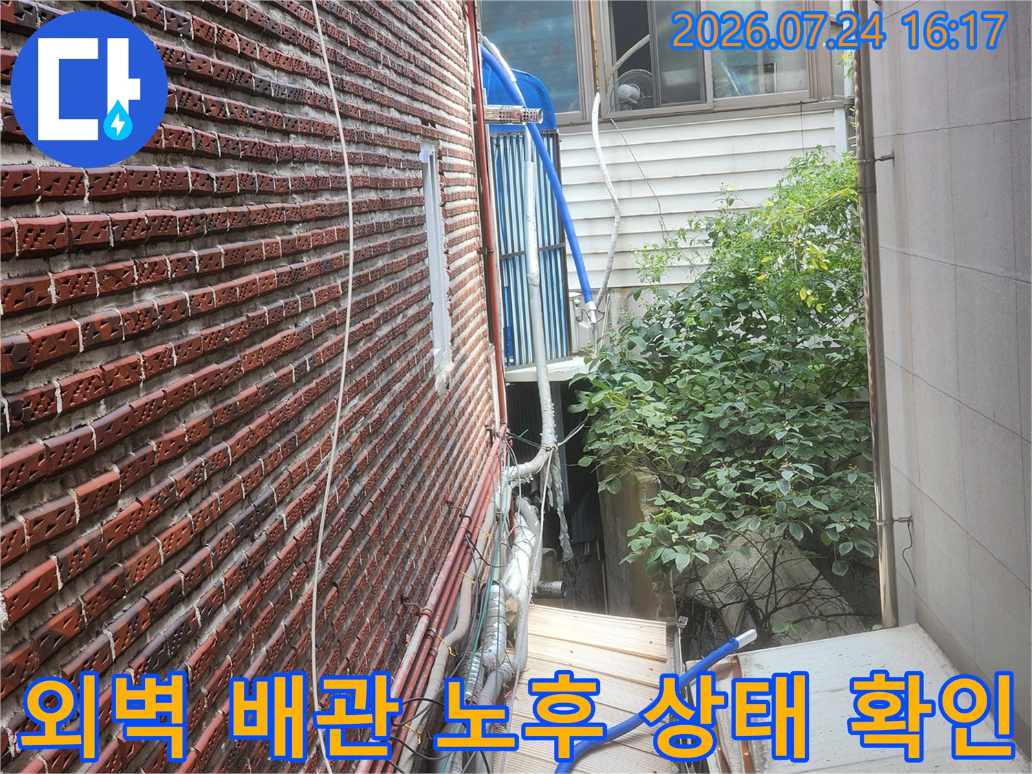 붉은 벽돌 외벽과 파란색 보온재로 감싸진 수도 배관 점검 장면