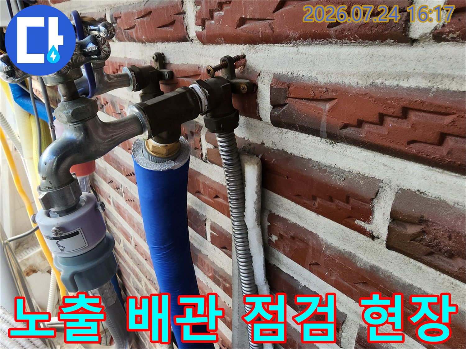 붉은 벽돌 외벽에 노출된 파란색과 은색 단열재 배관 및 밸브 점검