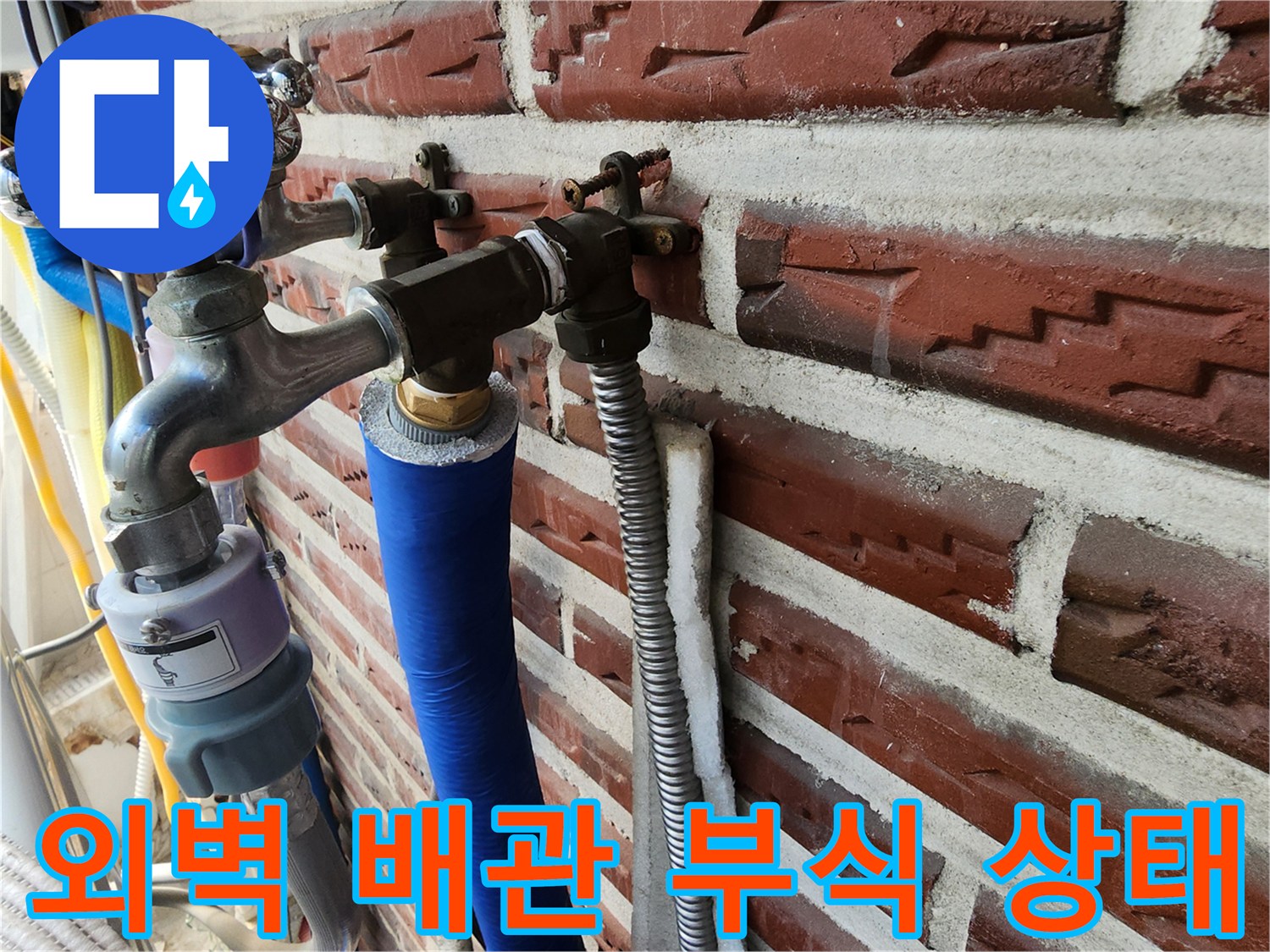 붉은 벽돌 외벽에 설치된 수도꼭지와 파란색 보온재가 씌워진 배관입니다.