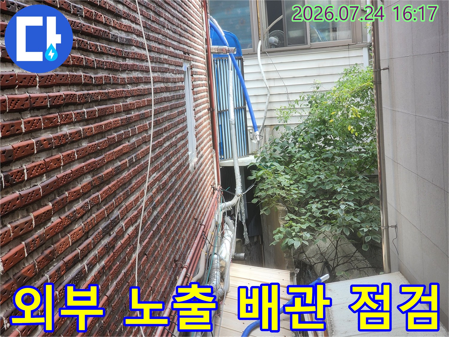 붉은 벽돌 외벽에 설치된 파란색 보온재 배관과 금속 배관 상태 확인