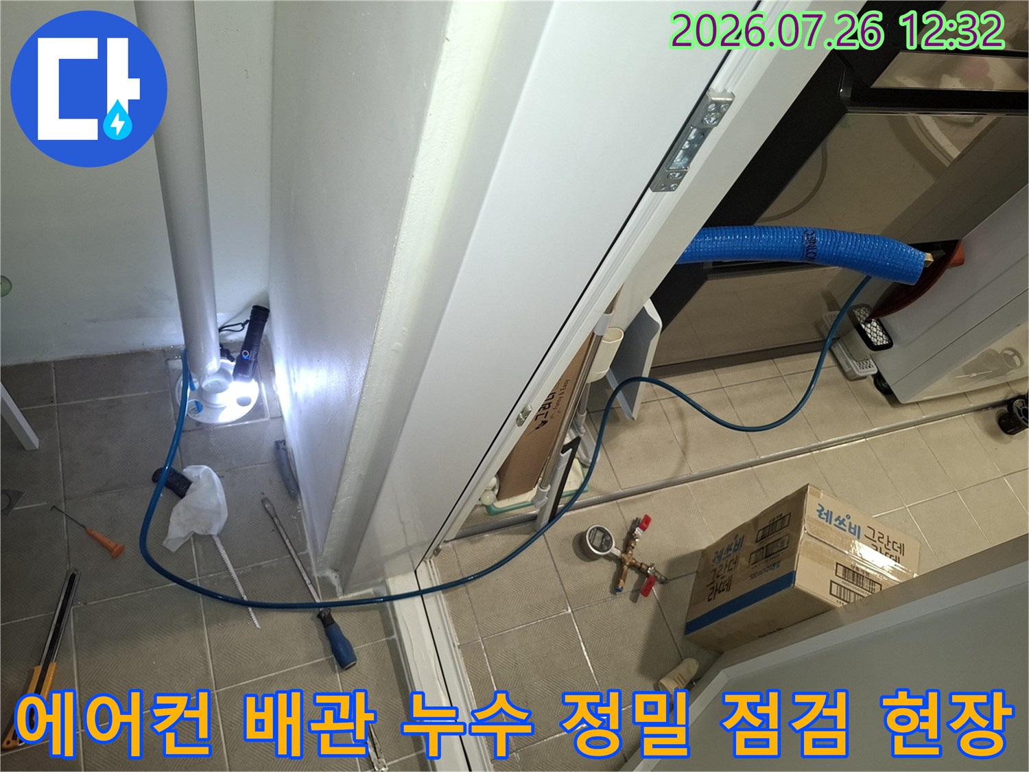 흰색 벽체 옆으로 파란색 주름관과 측정 장비가 연결된 에어컨 배관 누수 점검 모습