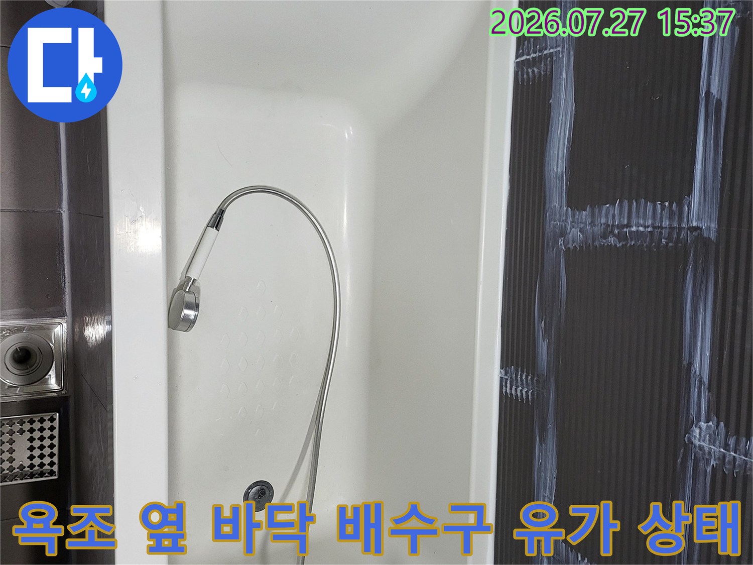 샤워 호스가 놓여 있는 욕조와 하단에 설치된 스테인리스 재질의 바닥 배수구-유가