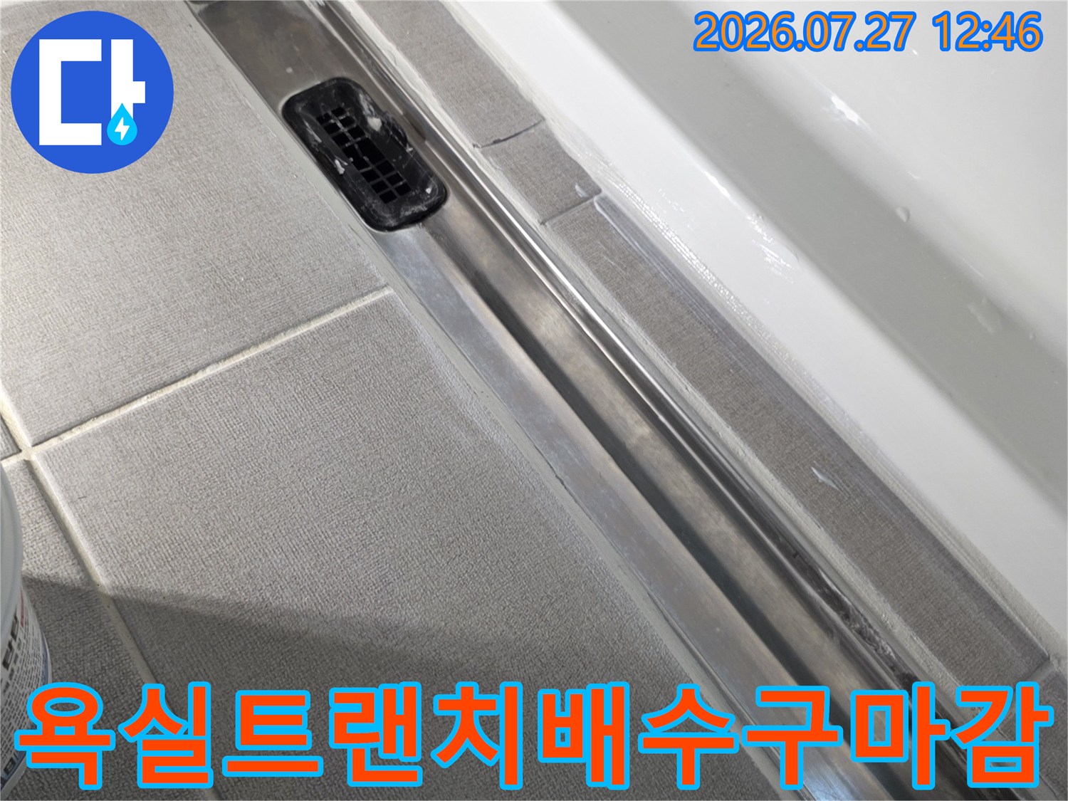회색-타일-바닥에-설치된-긴-직사각형-금속-배수구와-검정색-거름망