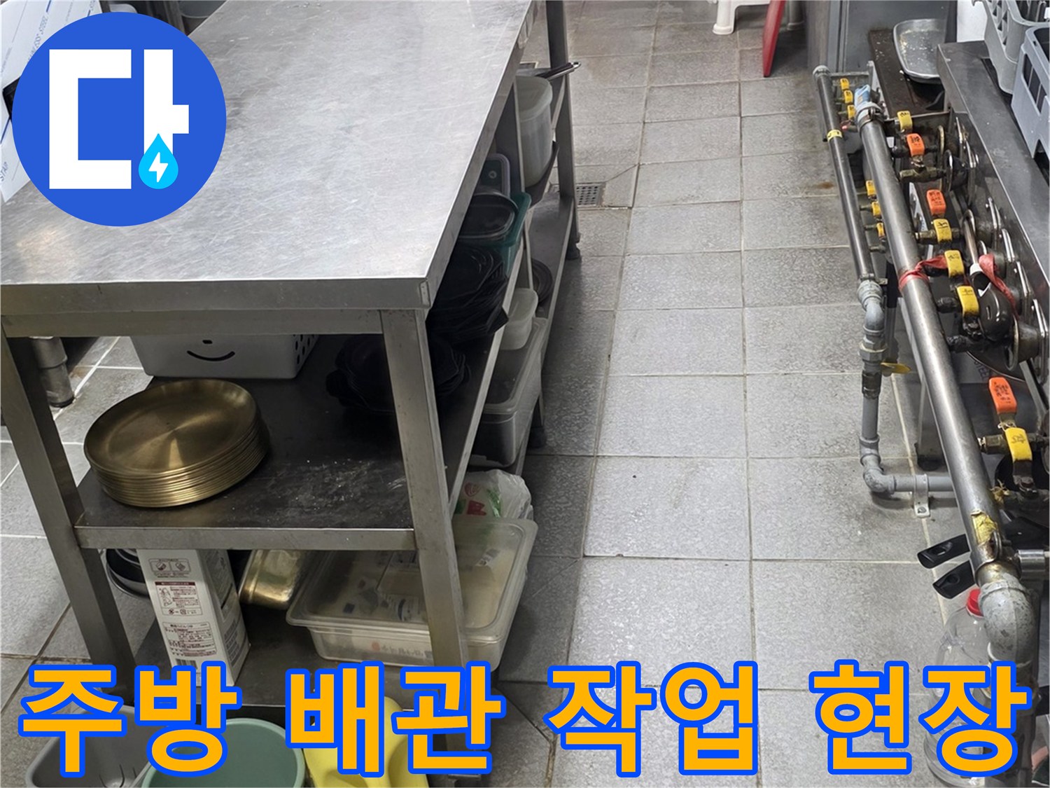 상업용 주방의 스테인리스 선반 아래에 놓인 배관 보수용 자재와 도구들