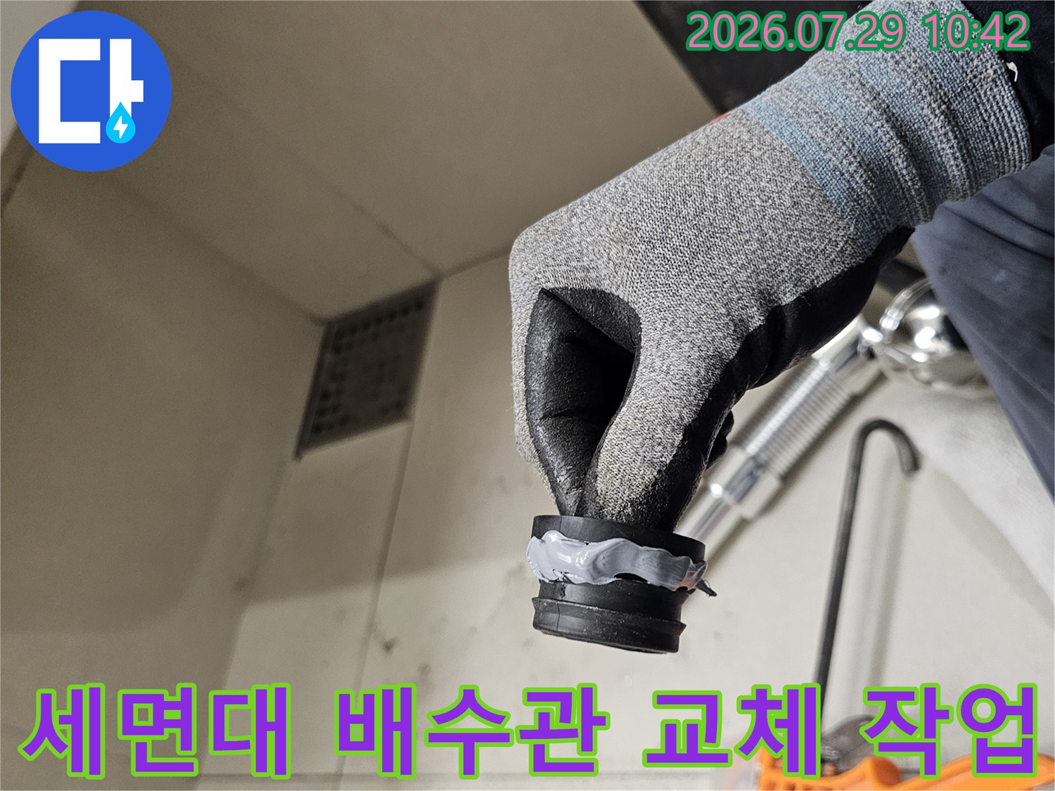 장갑을 낀 채로 세면대 아래쪽의 노후된 배수 트랩과 연결 부위를 점검하는 모습