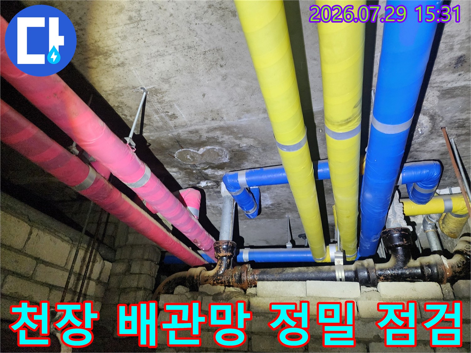 화장실 천장 상부에 배치된 여러 색상의 배관 시스템을 촬영한 사진입니다.