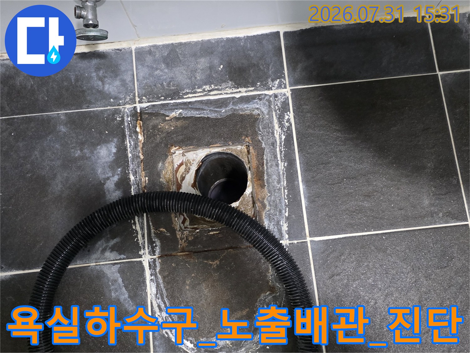 욕실 바닥 타일이 제거된 하수구 주변의 노출된 배관과 진단용 호스가 연결된 모습