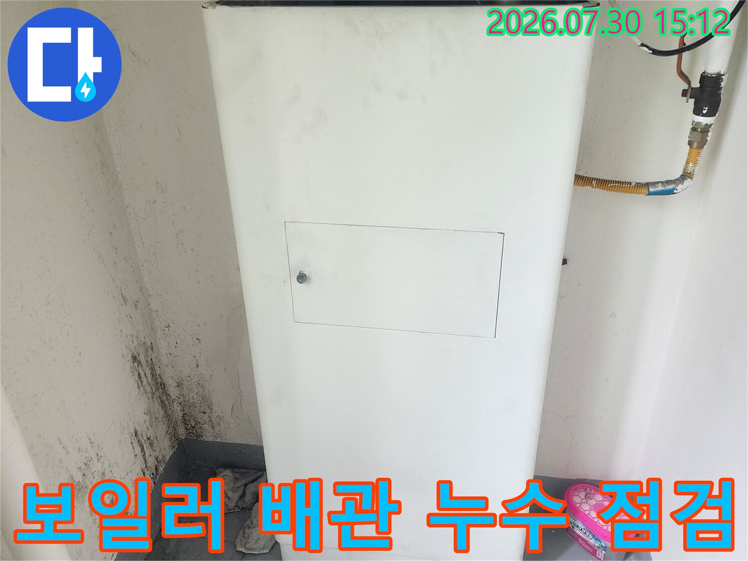 보일러실 내부에 배치된 대형 온수기 장비와 연결된 배관 시스템을 점검하는 모습