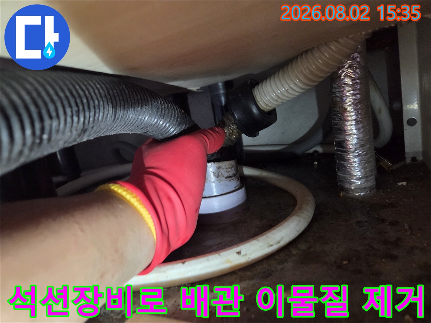빨간색 장갑을 착용하고 석션기를 사용하여 싱크대 하부 배관 내부를 청소하는 모습