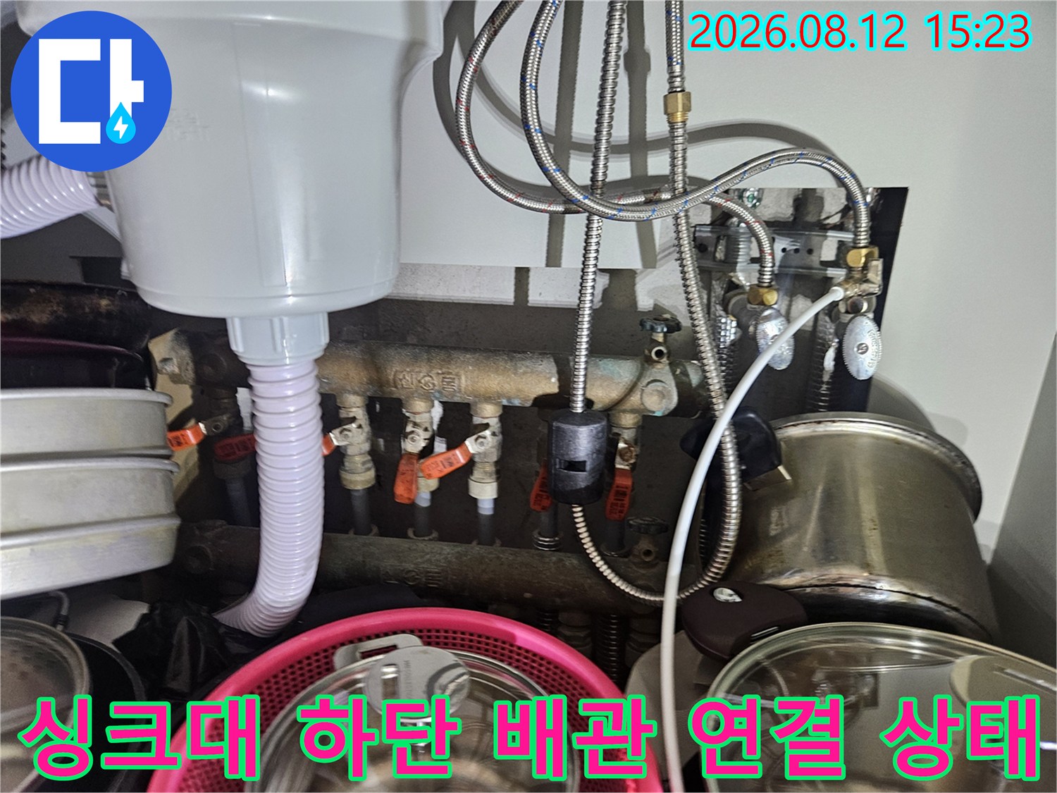 싱크대 아래 설치된 흰색 정수기 필터와 금속제 유연한 배관들이 얽혀 있는 모습