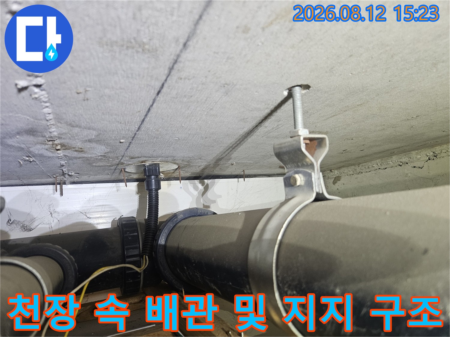 콘크리트 천장에 고정된 검은색 하수 배관과 금속제 지지대-전체 모습