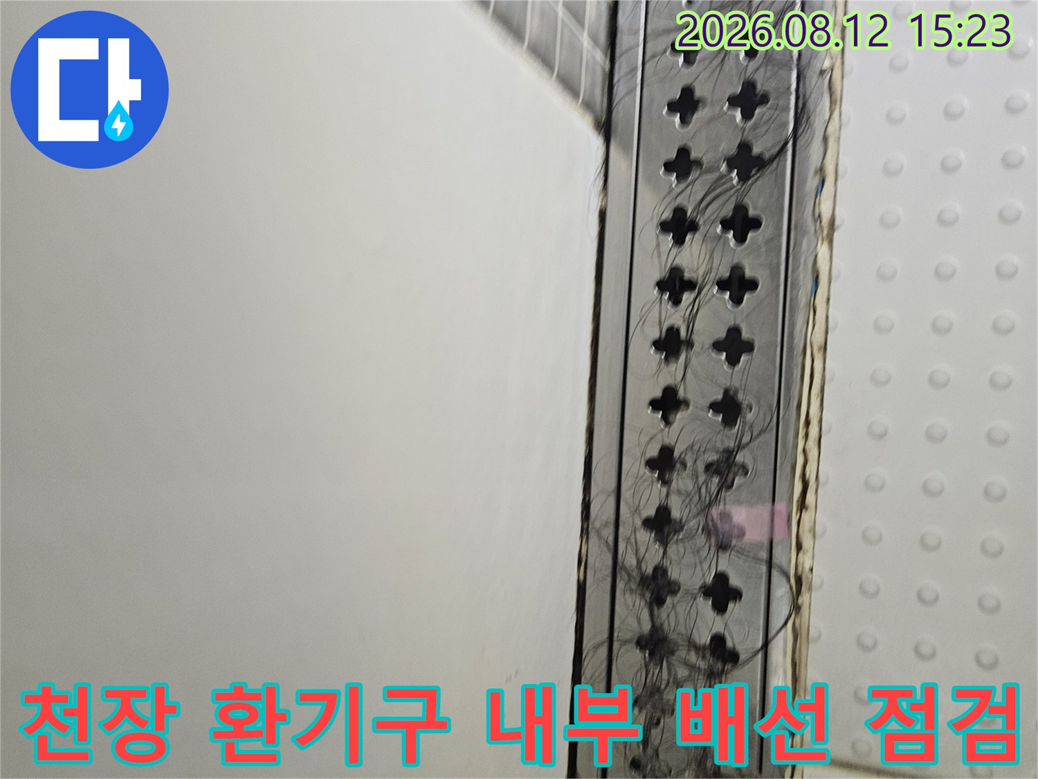 흰색 천장 패널과 검은색 환기 그릴 사이로 삐져나온 전선들의 모습