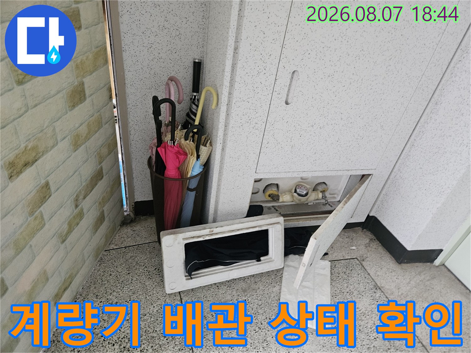 아파트 계량기함 내부의 수도 밸브와 연결된 배관을 점검하는 장면입니다.