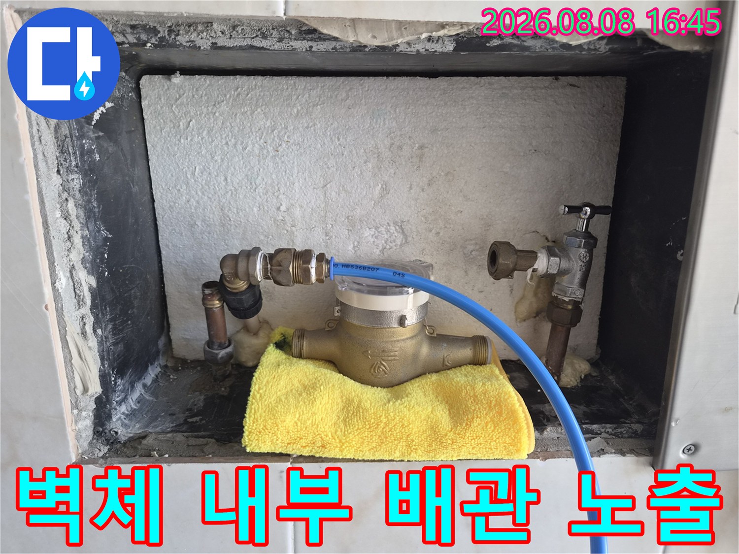 타일이 제거된 벽면 안쪽에 드러난 수전 연결 부속과 점검 장비의 모습입니다.