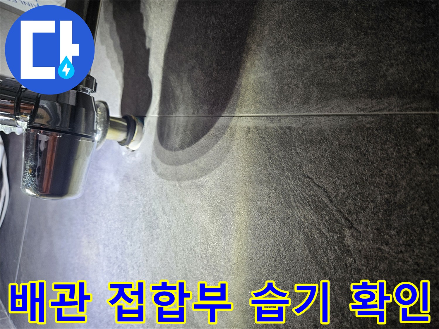어두운 색상의 타일 벽면에 위치한 금속 배관 부위