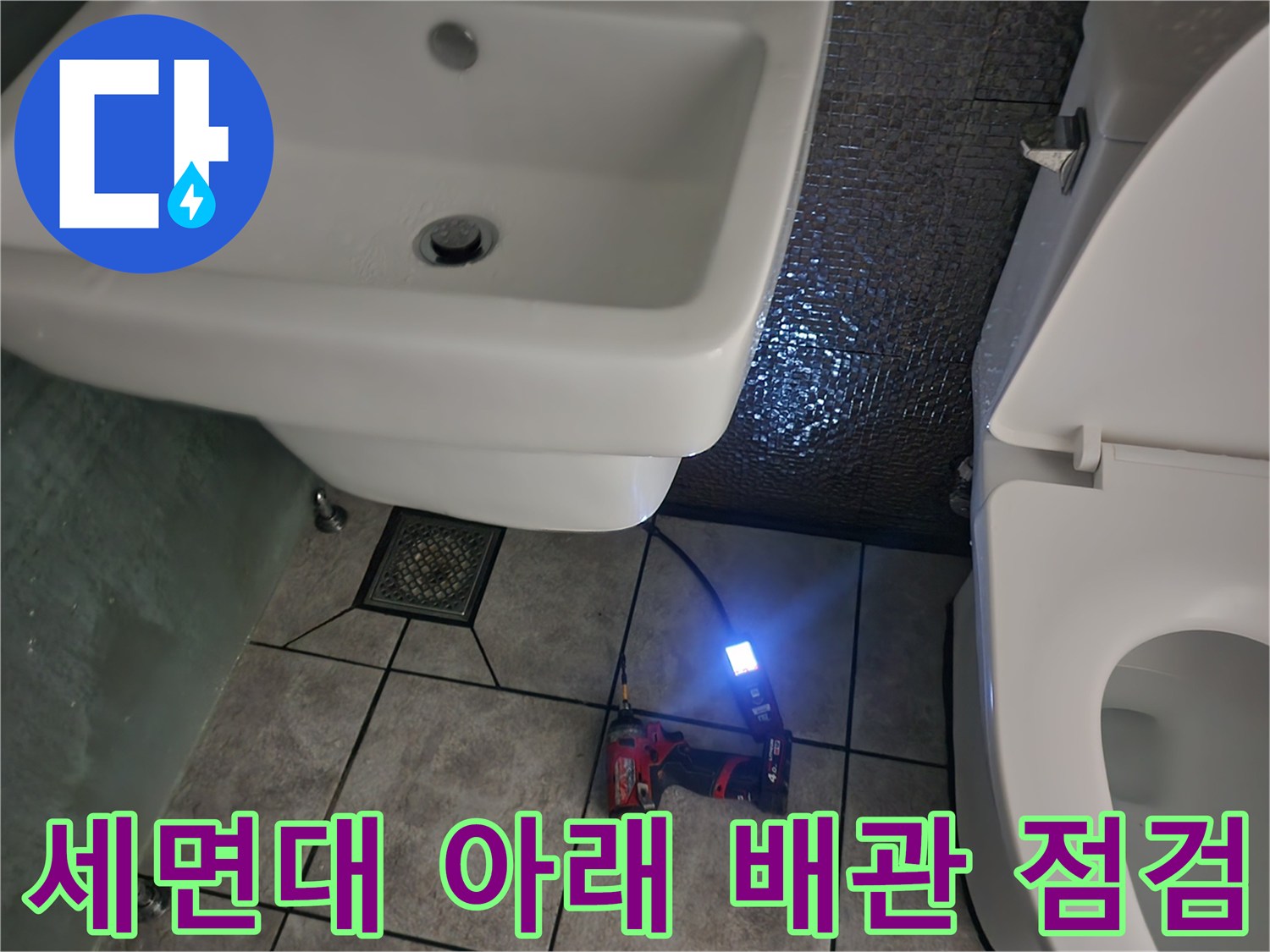 세면대와 변기 사이 바닥 타일 부근에서 진행 중인 배관 점검 작업