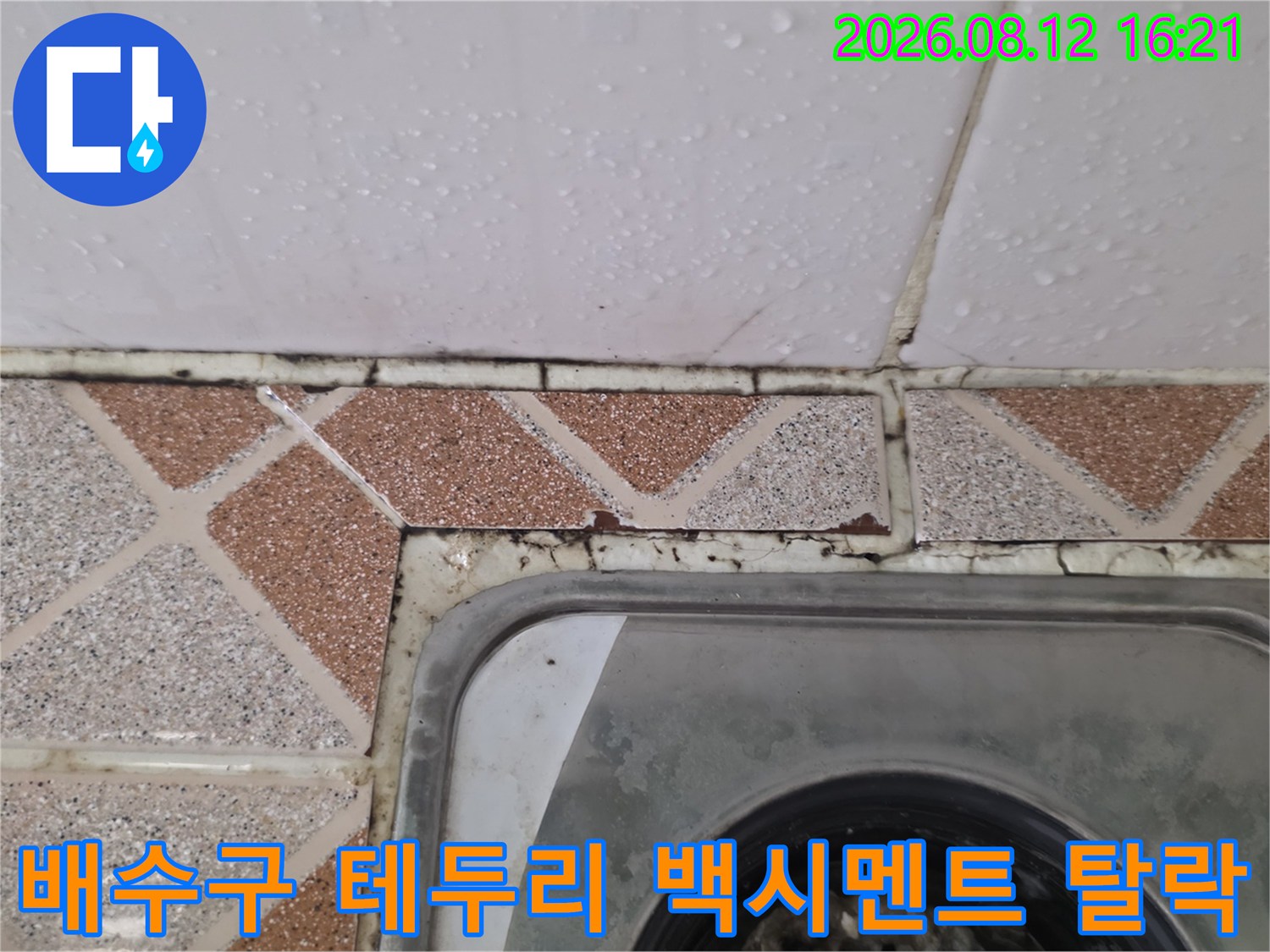 금속 재질의 욕실 배수구 주변 타일 마감재가 떨어져 검은 틈새가 보이는 사진