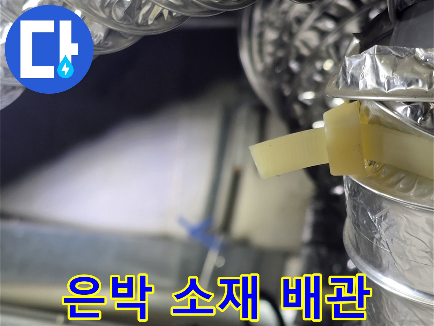 천장 구조물 내부에 노출된 은박 재질의 덕트 배관을 촬영한 사진입니다.