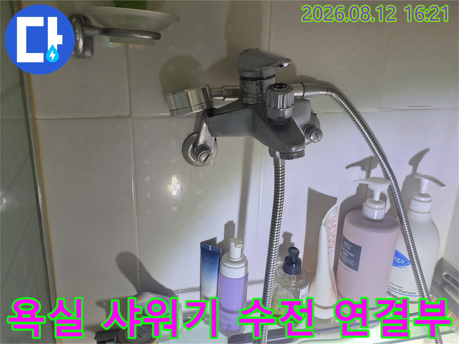 흰색 타일 벽면에 설치된 은색 샤워기 수전과 배관 연결 부위-사진